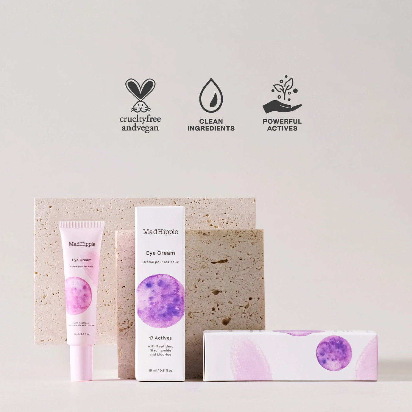 MadHippie eye cream tube in blush pink and white box with purple watercolor circle displayed against textured stone blocks