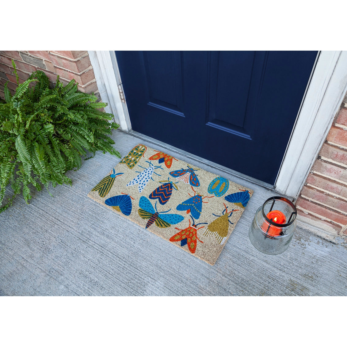Coir doormat with colorful mushroom pattern in blue, orange, yellow and green tones on gray porch with navy door