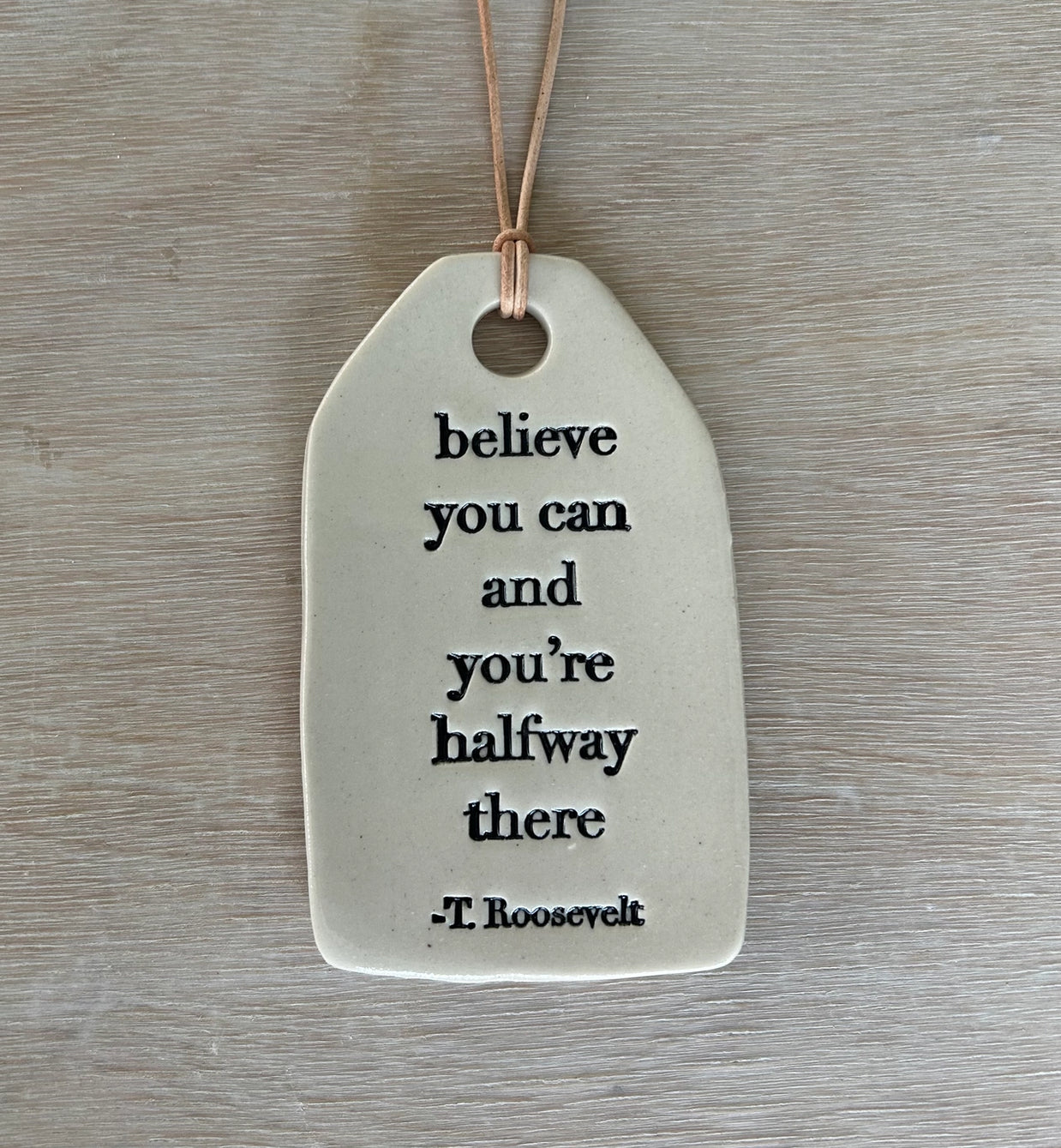 Decorative ceramic tag with inspirational quote on a wooden surface