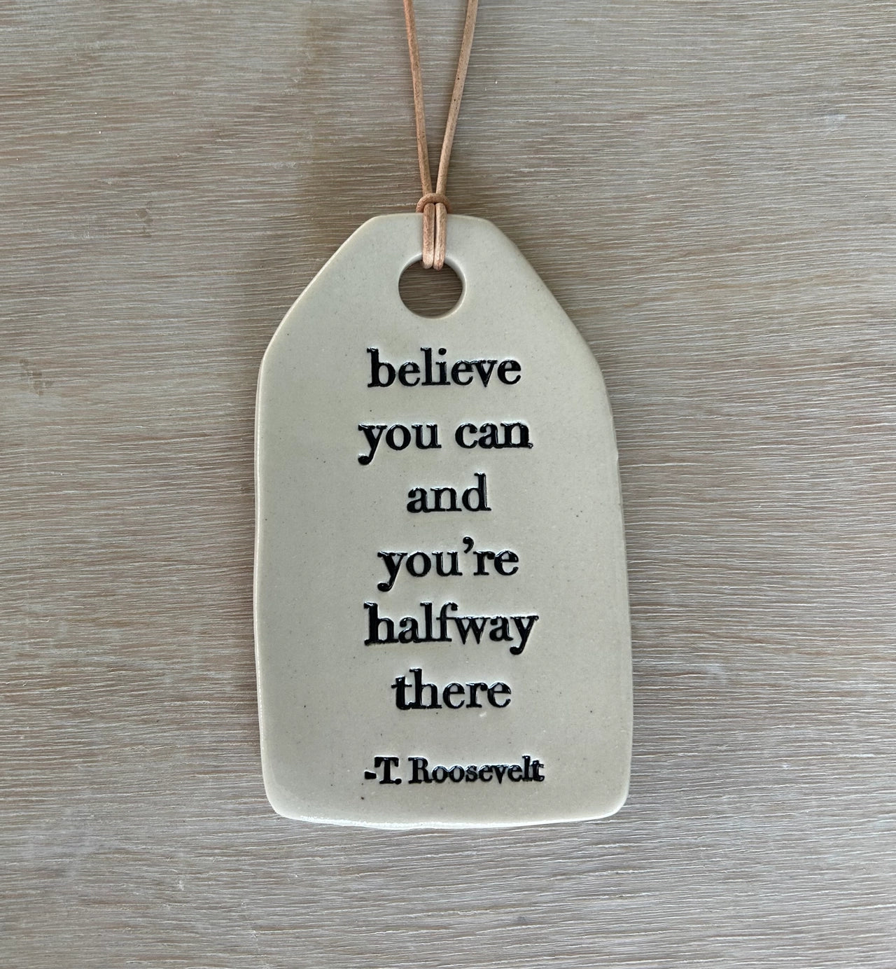 Decorative ceramic tag with inspirational quote on a wooden surface