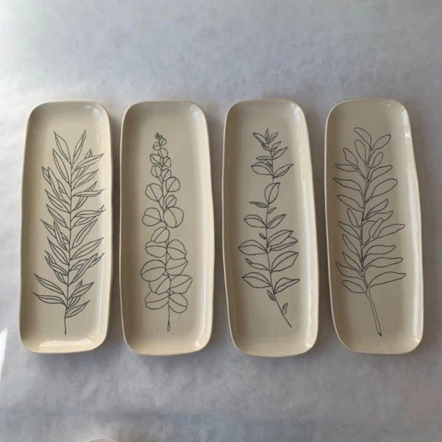 Four rectangular ceramic trays in cream glaze with hand-drawn botanical line art of different leafy stems and sprigs