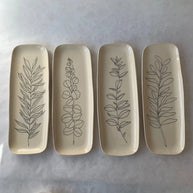 Four rectangular ceramic trays in cream glaze with hand-drawn botanical line art of different leafy stems and sprigs