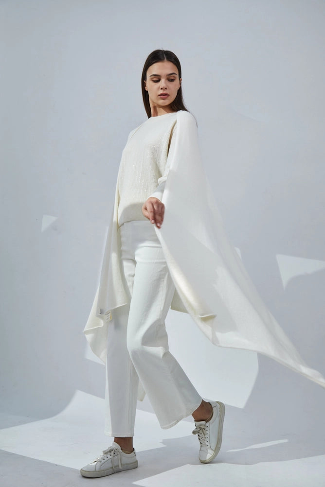 Ivory cable-knit sweater with dramatic flowing side panel drape worn with white pants and cream leather sneakers