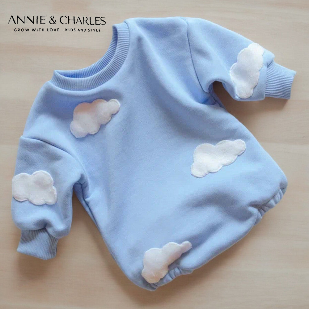 Sky blue fleece children's sweatshirt with white puffy cloud appliqués and ribbed cuffs on light wood surface