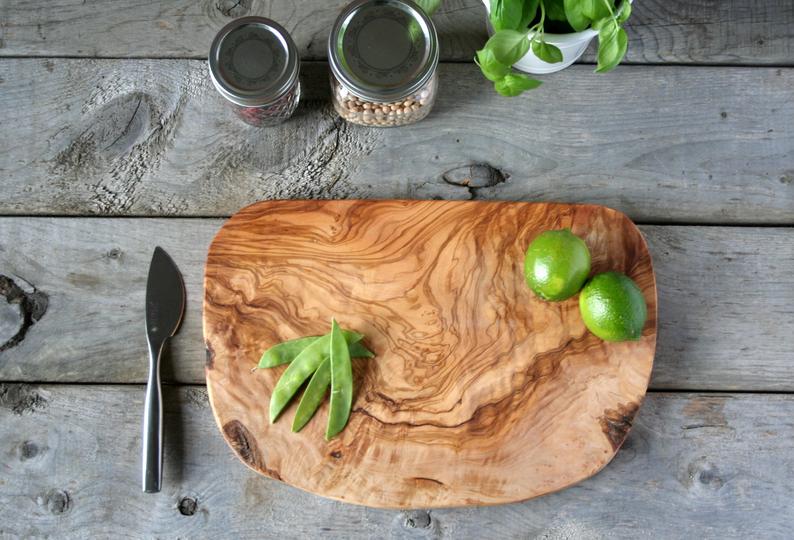 Olive wood cutting board with natural grain patterns holding fresh limes and snap peas on weathered gray wood surface