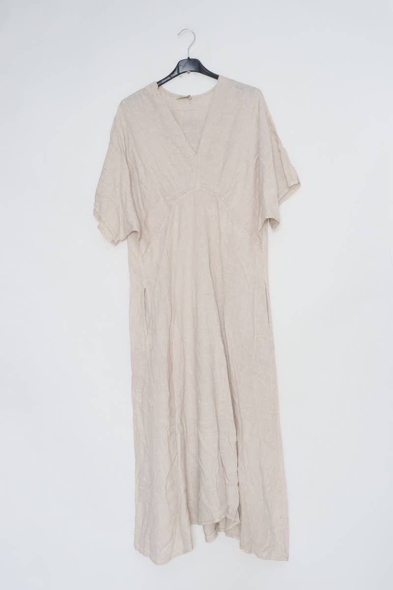 Natural linen caftan dress with v-neck, kimono sleeves, empire waist and flowing maxi length on hanger against white wall