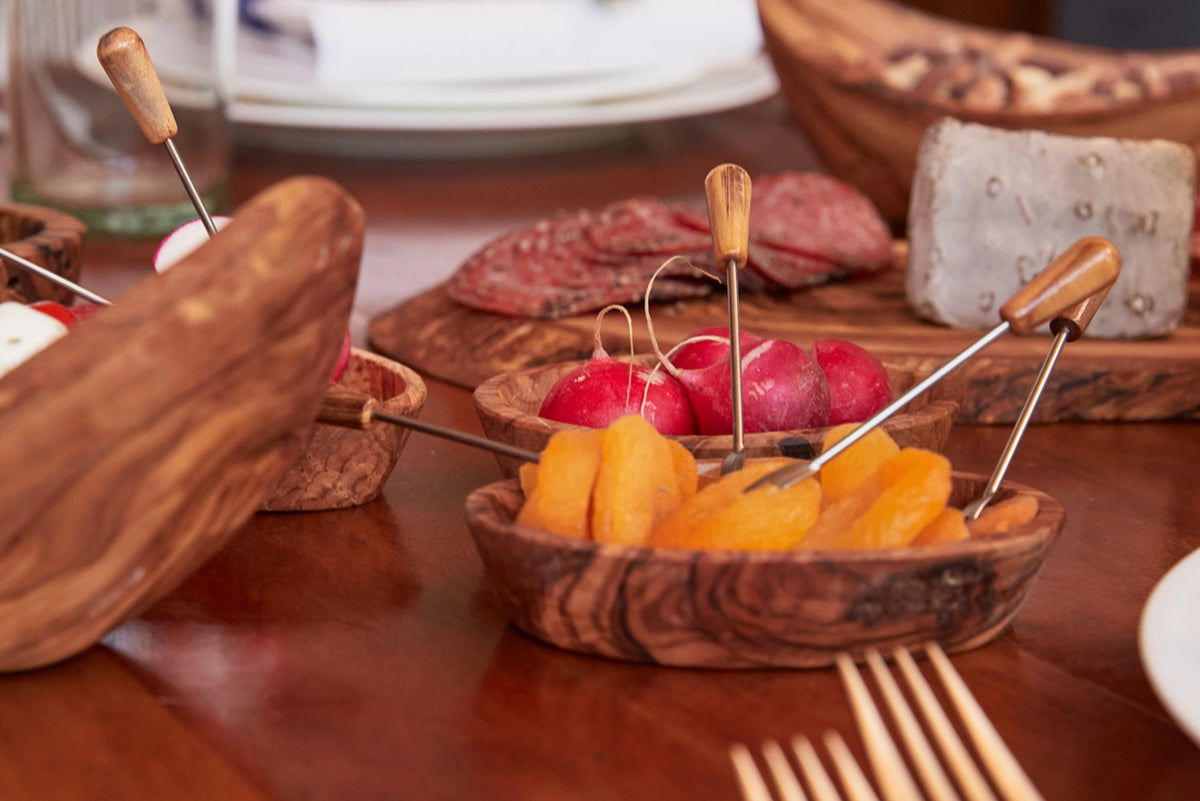 Wooden appetizer bowls with cheese cubes and pickled vegetables pierced with cocktail picks on charcuterie board