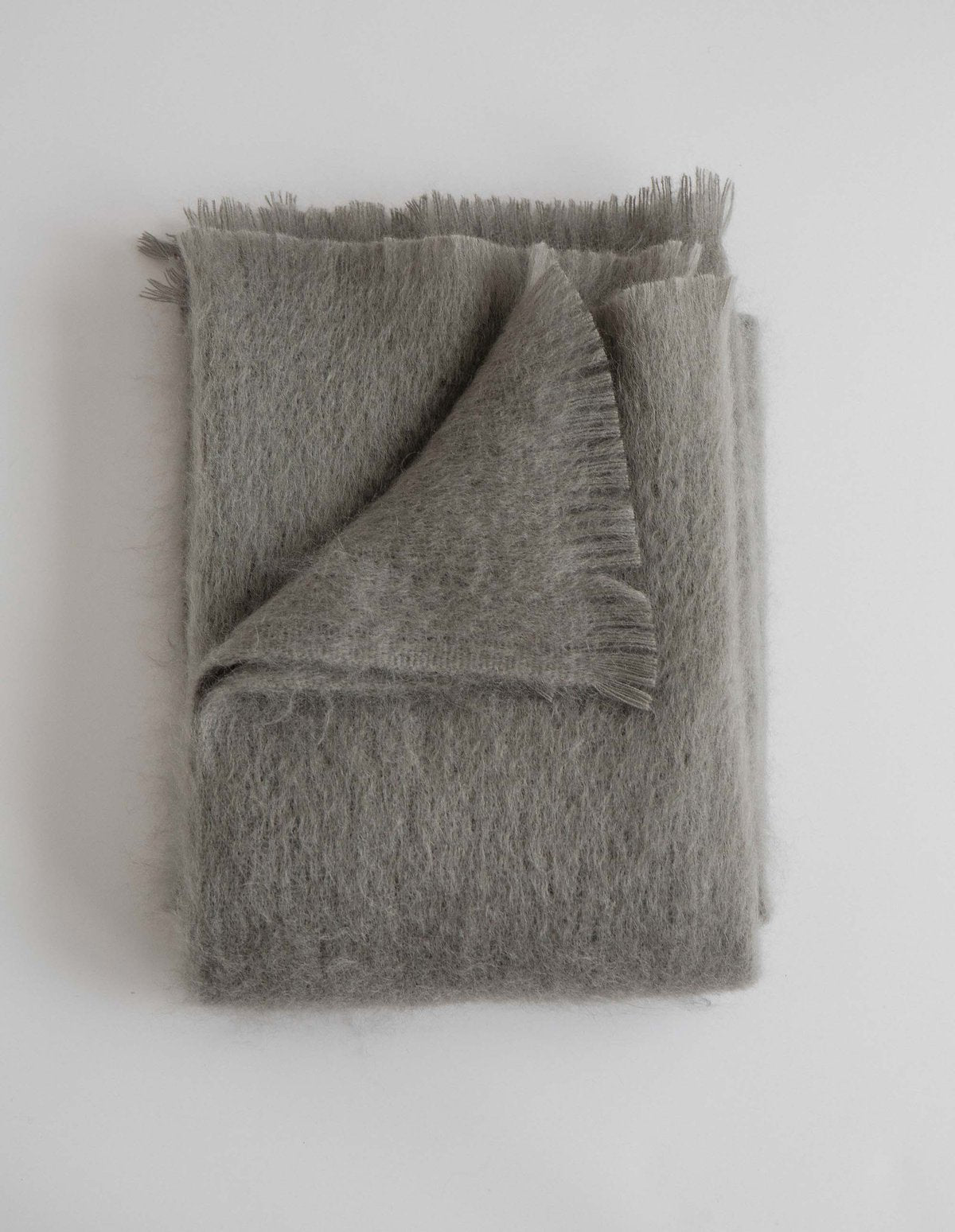 Folded mohair or alpaca throw blanket in heathered gray with brushed fringe edges on white background
