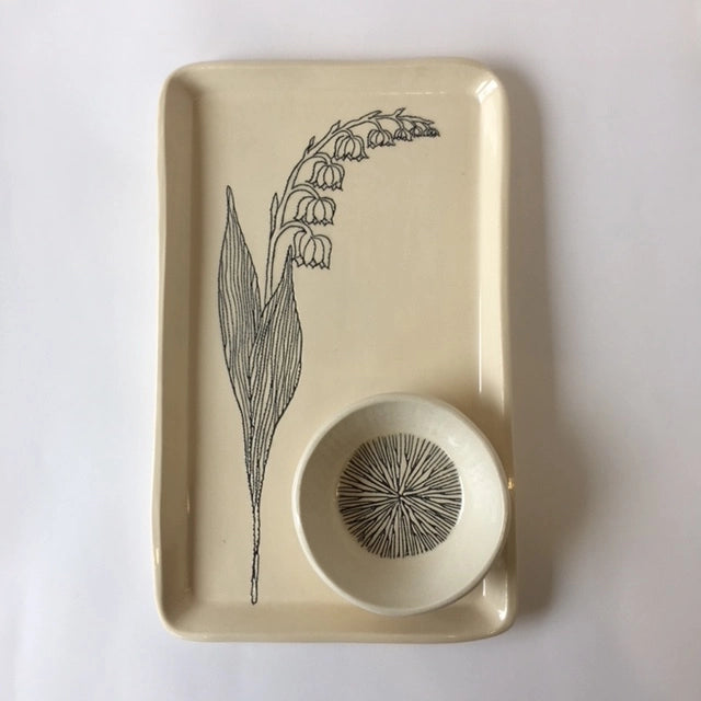 Cream ceramic tray with black line drawing of lily of the valley flower and matching circular bowl with starburst pattern