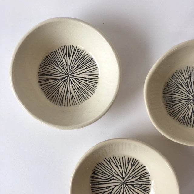 Cream ceramic bowls with hand-drawn black starburst pattern radiating from center, viewed from above on white surface
