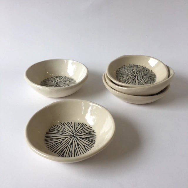 Set of four cream ceramic bowls with hand-drawn black radial starburst pattern in center on white surface