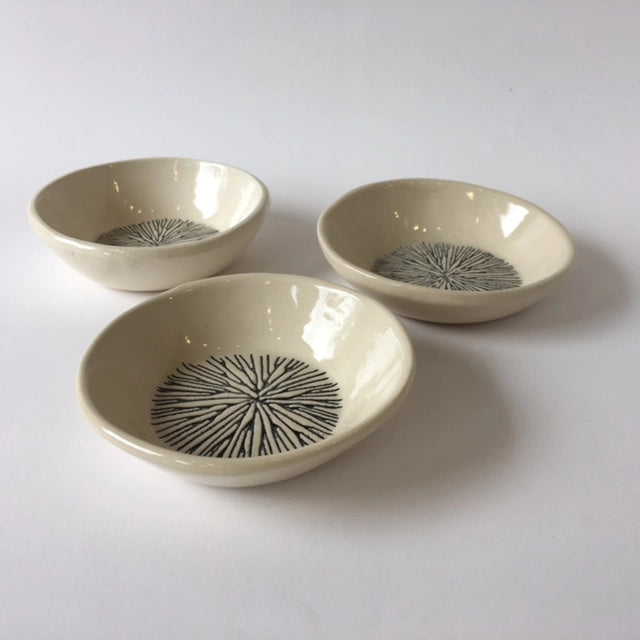 Set of three cream ceramic bowls with hand-drawn black radiating starburst pattern in center on glossy glaze finish