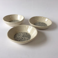 Set of three cream ceramic bowls with hand-drawn black radiating starburst pattern in center on glossy glaze finish