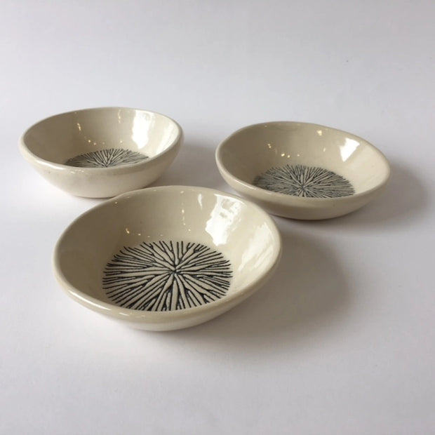 Set of three cream ceramic bowls with hand-drawn black radiating starburst pattern in center on glossy glaze finish