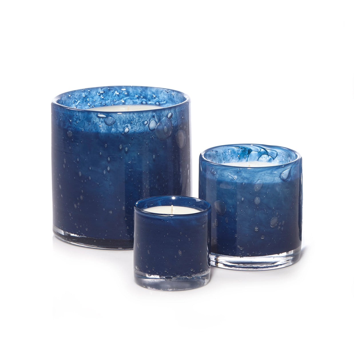 Three navy blue glass candle holders with bubble texture in graduated sizes filled with white wax on light background