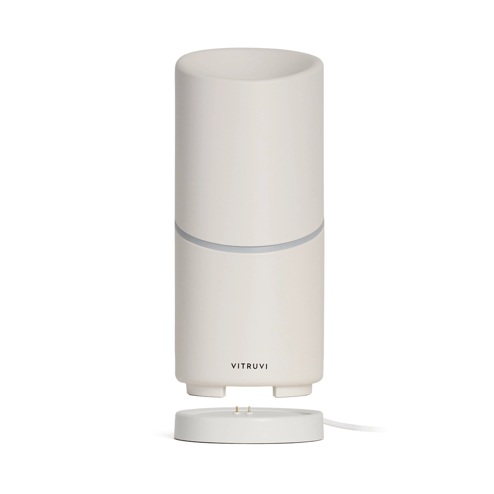White cylindrical essential oil diffuser with gray accent band and charging base, Vitruvi branding on lower section