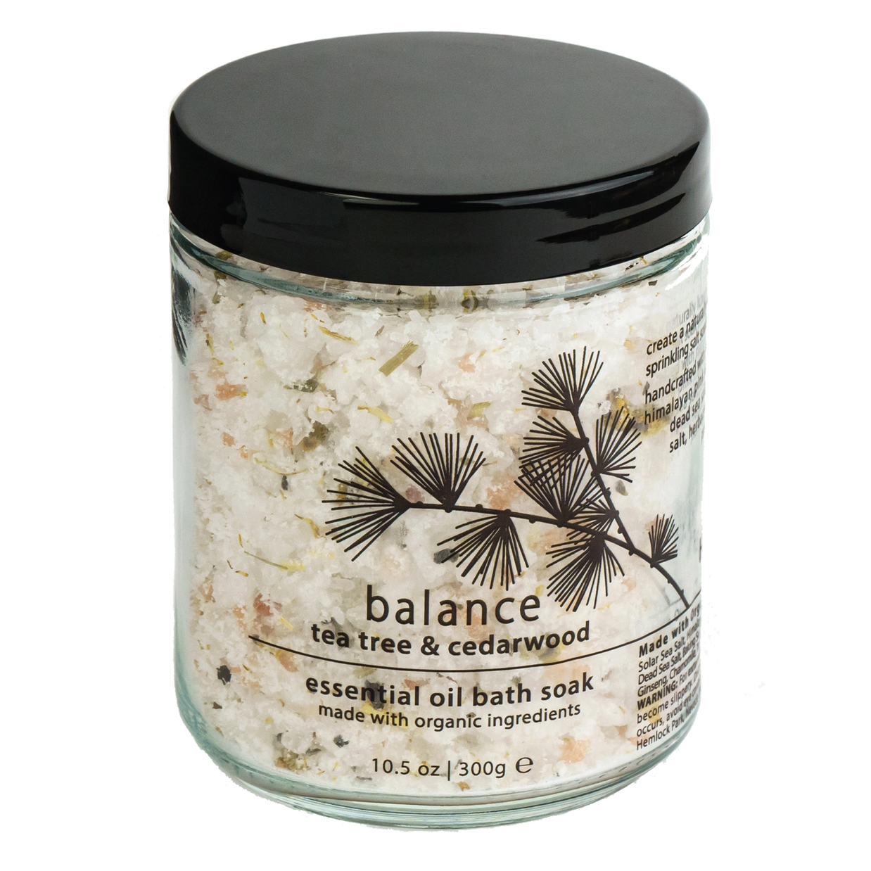 Clear glass jar with black lid containing white crystalline bath salts with herbs, labeled Balance tea tree & cedarwood