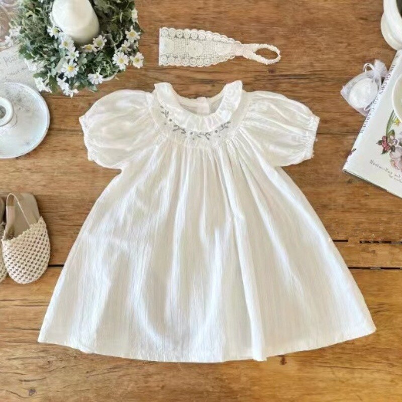 White cotton christening dress with puffed sleeves, smocked neckline, and gathered bodice on rustic wood surface