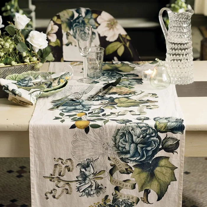 Linen table runner with vintage botanical print featuring blue roses, green leaves, and yellow fruit on white background