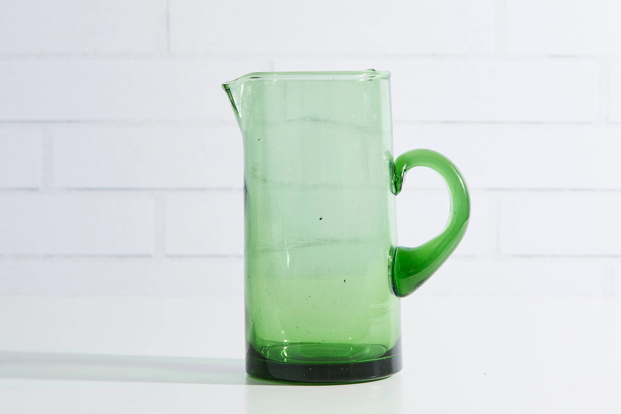 Transparent green glass pitcher with curved handle and pouring spout, featuring darker green base and organic bubbles