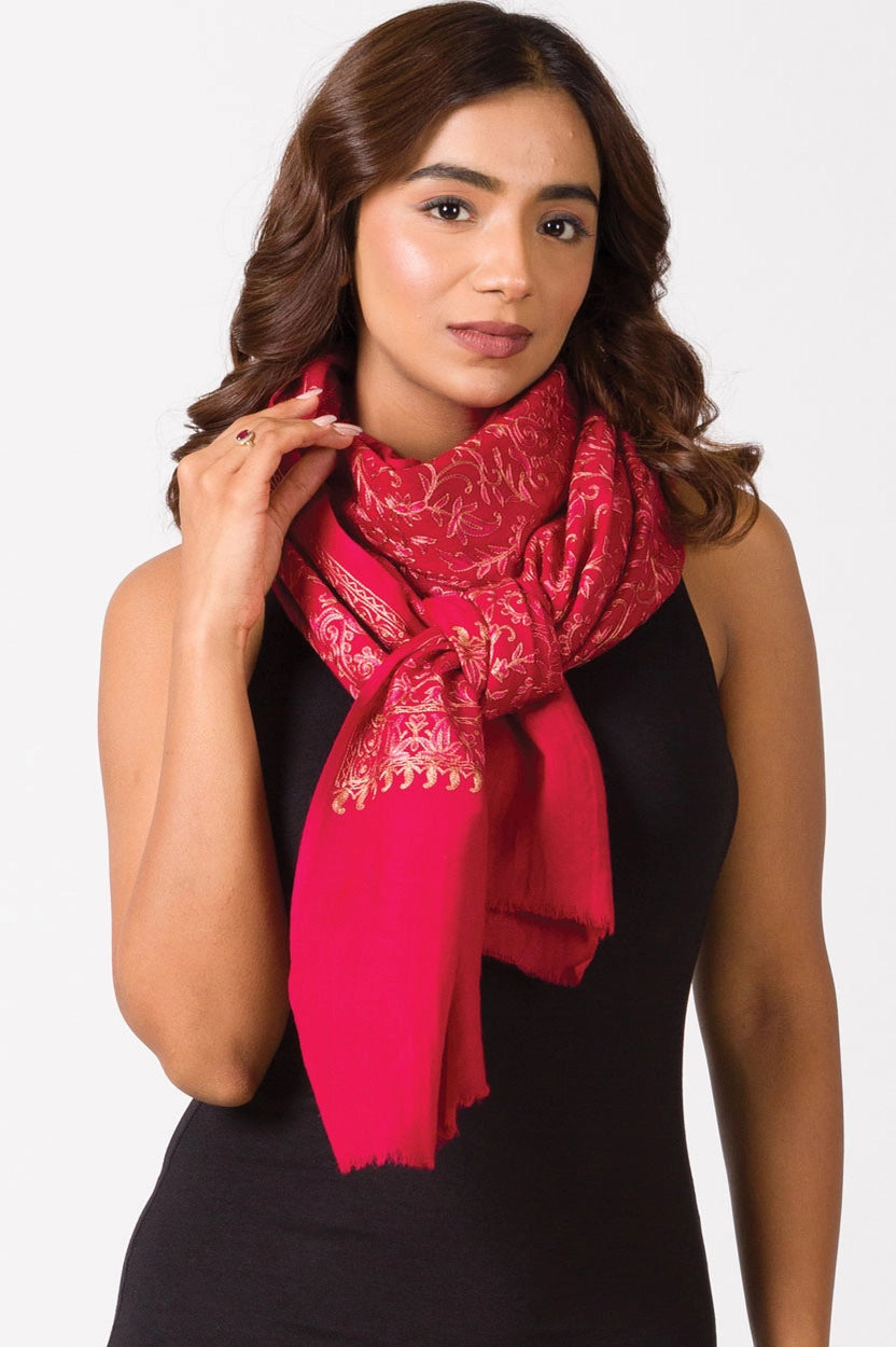 Vibrant red silk scarf with gold metallic floral embroidery and frayed edges draped around neck on black top