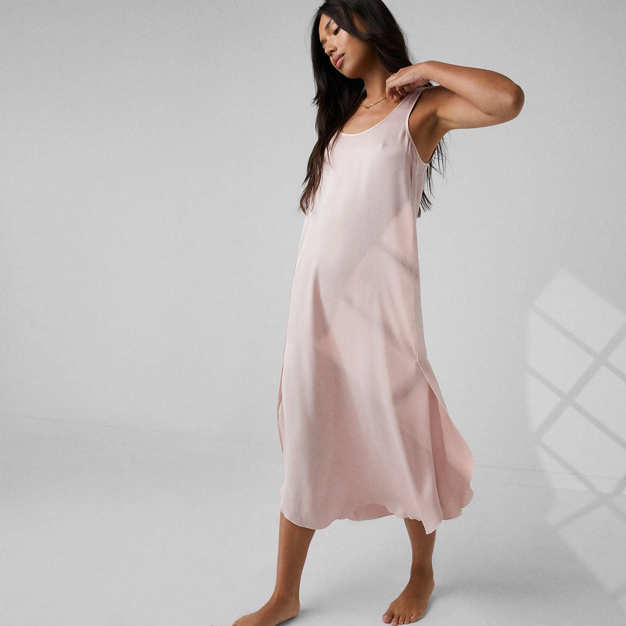 Soft pink silk slip dress with scoop neckline and midi length flowing A-line silhouette on gray background