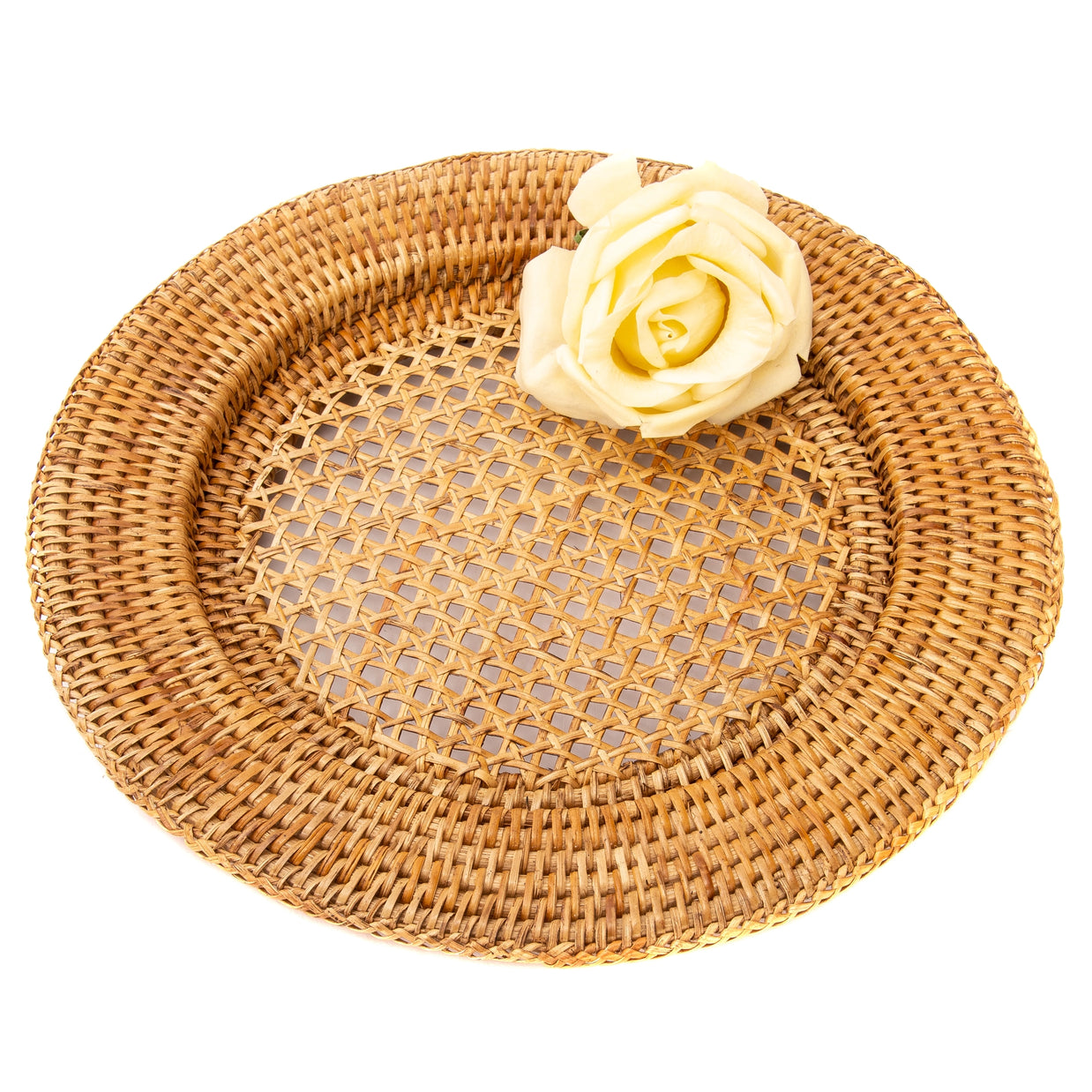 Round woven rattan charger plate in honey brown with raised rim and open lattice center, cream rose accent on edge