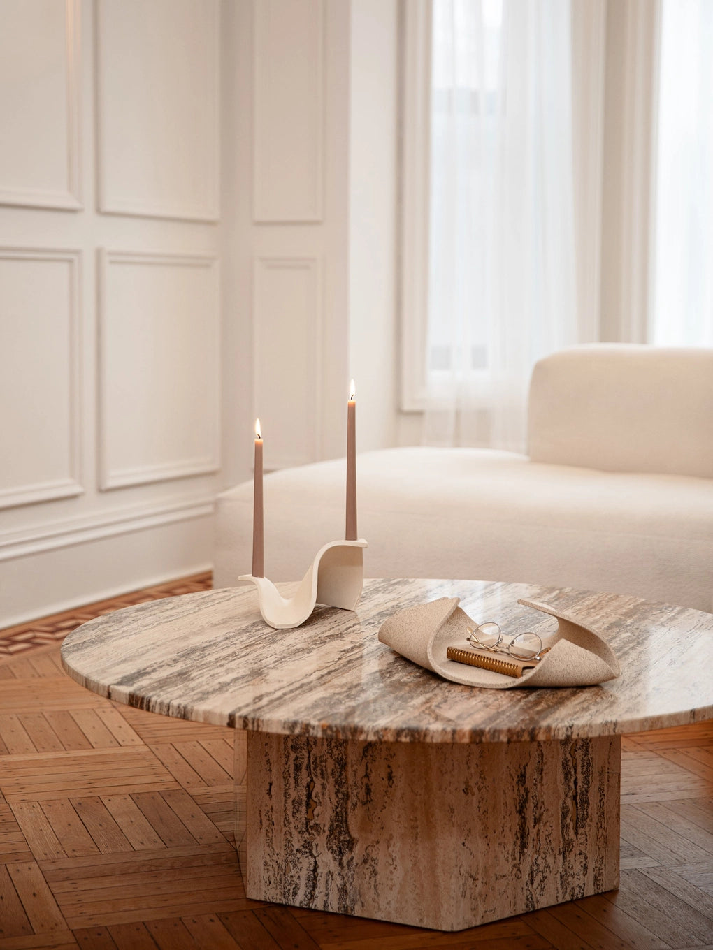Travertine stone coffee table with natural veining, holding cream ceramic candleholder with lit tapers and catch-all tray