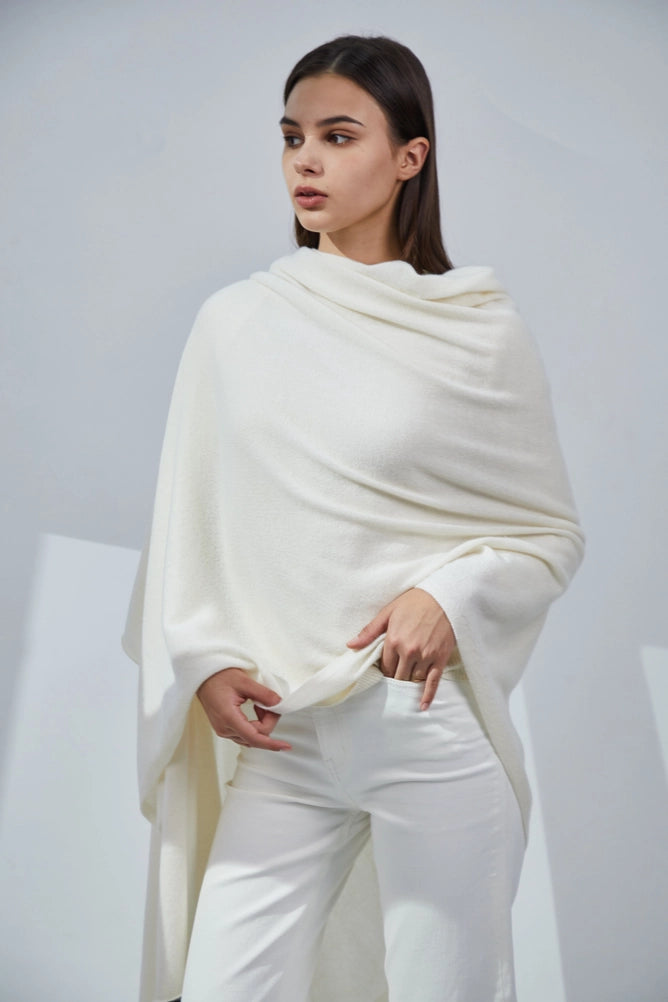 Cream white cashmere wrap shawl draped across shoulders over fitted white turtleneck and trousers in minimalist setting