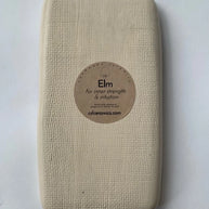 Cream rectangular ceramic tray with textured linen-like surface and circular kraft paper label reading Elm on pale blue background