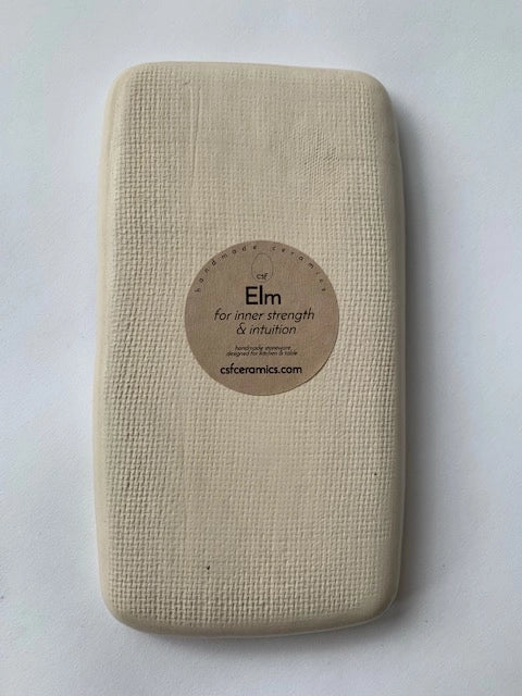 Cream rectangular ceramic tray with textured linen-like surface and circular kraft paper label reading Elm on pale blue background