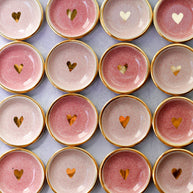 Ceramic ring dishes with gold rim in pink and cream glazes, each featuring hand-painted gold heart in center