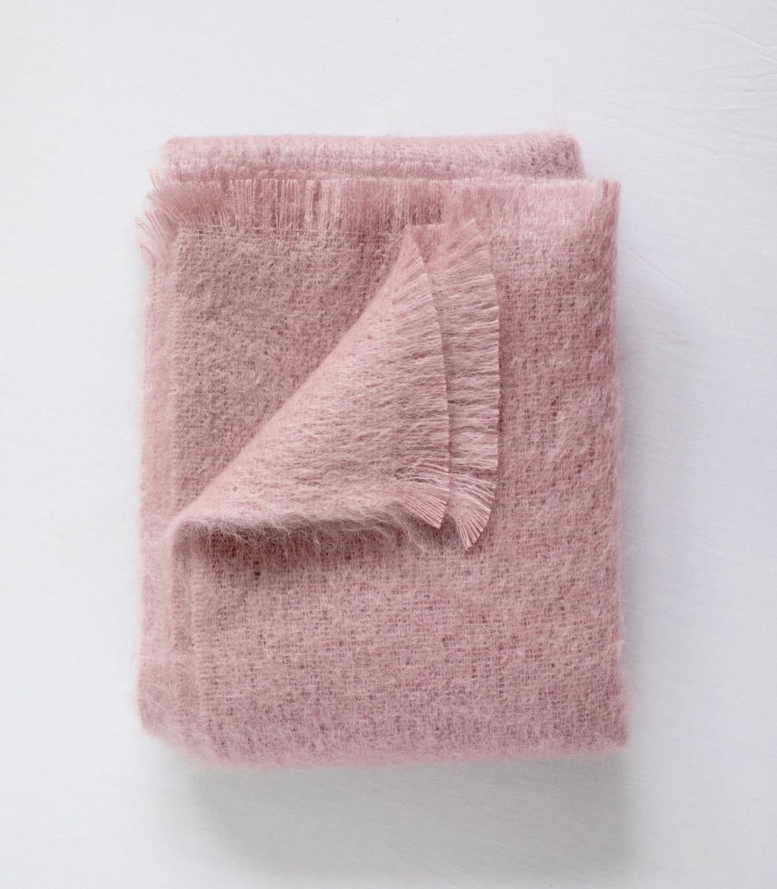 Folded dusty rose mohair throw blanket with fringed edges and soft fuzzy texture on white background