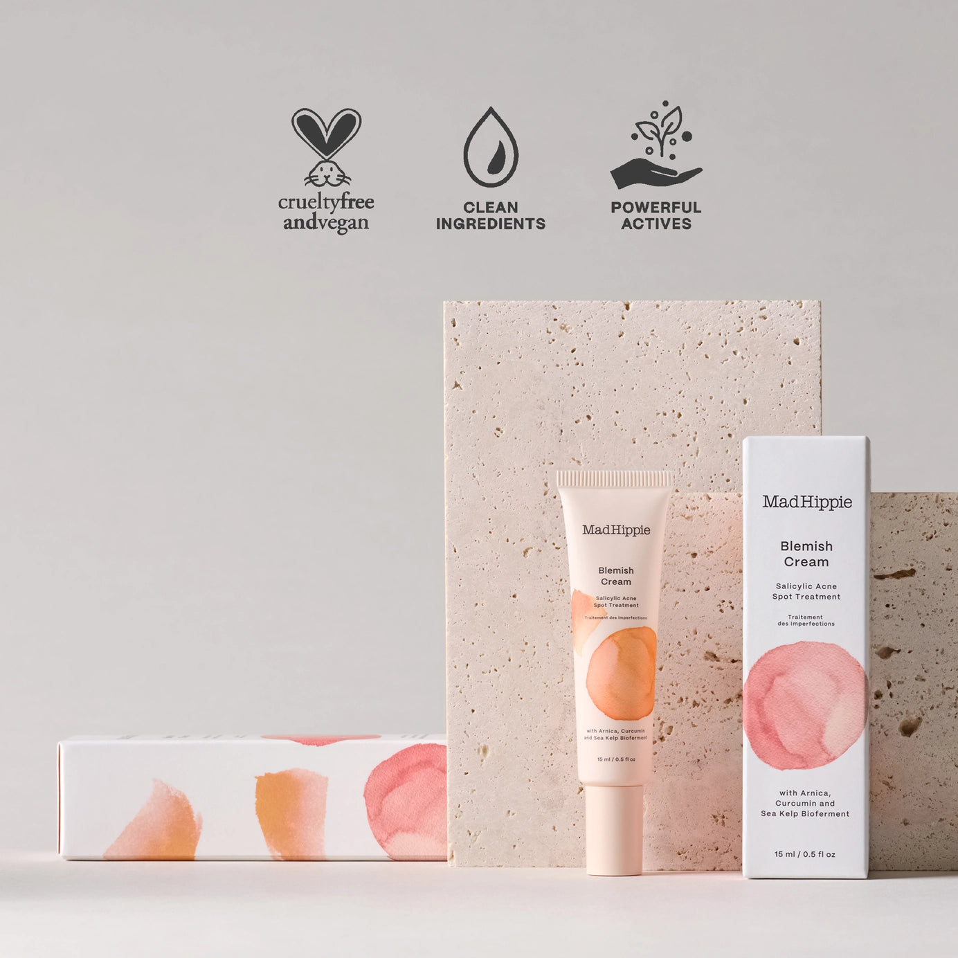 MadHippie Blemish Cream tube and box with watercolor peach and pink circles, displayed against textured stone backdrop