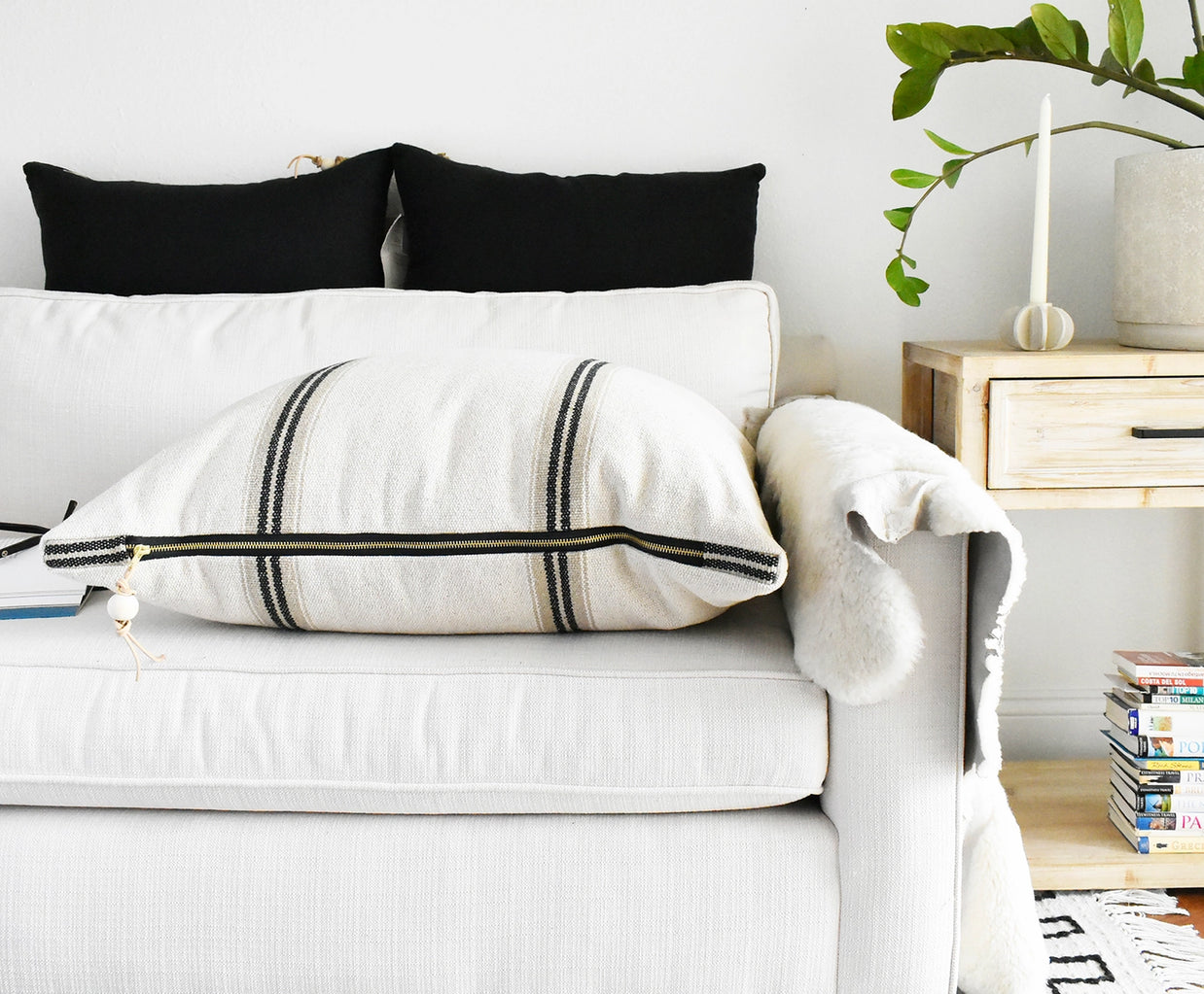 Cream linen lumbar pillow with black woven stripes and brass zipper detail on white sofa with black accent pillows