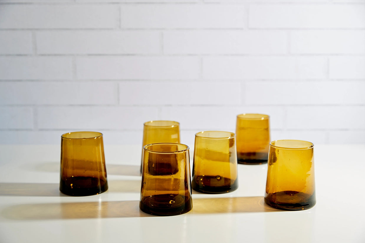 Set of five amber glass tumblers with gradient ombre effect from golden honey to dark brown base on white surface