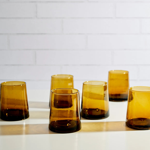 Set of five amber glass tumblers with gradient ombre effect from golden honey to dark brown base on white surface
