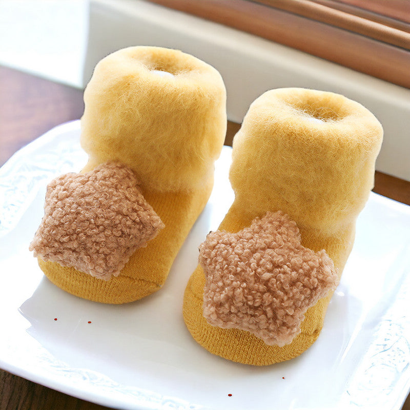 Plush baby booties in mustard yellow fleece with fuzzy pom-pom appliques and non-slip textured soles on white plate