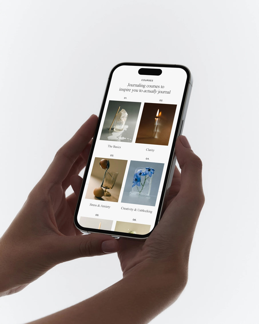 Hands holding black-framed smartphone displaying journaling course catalog with minimalist photography grid layout