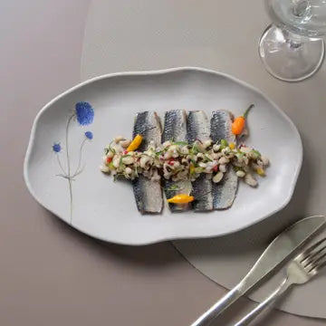 Rolled herring fillets with diced vegetable medley garnished with orange zest and blue flower on white ceramic plate