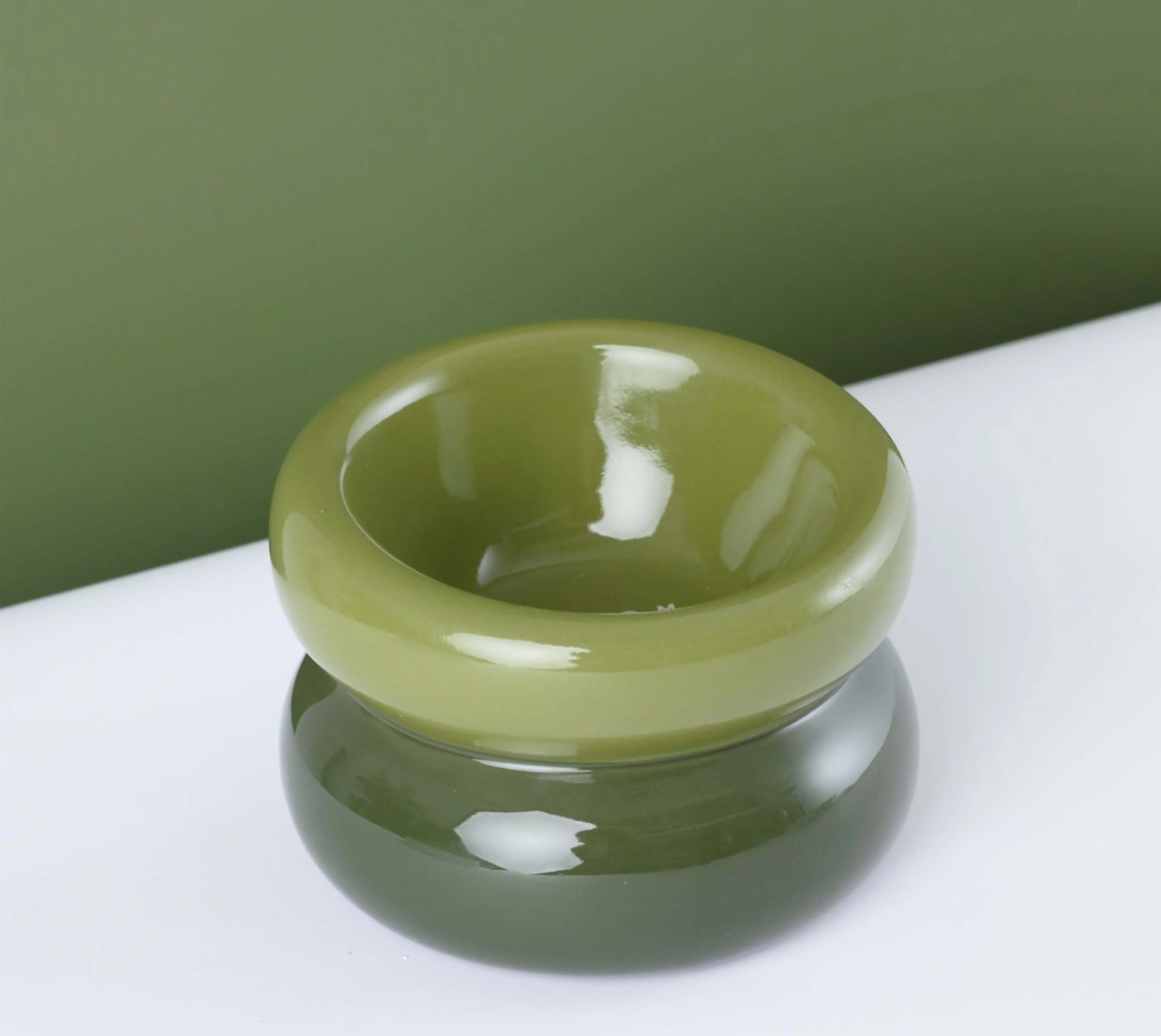 Glossy olive green ceramic bowl with smooth rounded edges and wide shallow interior on white surface