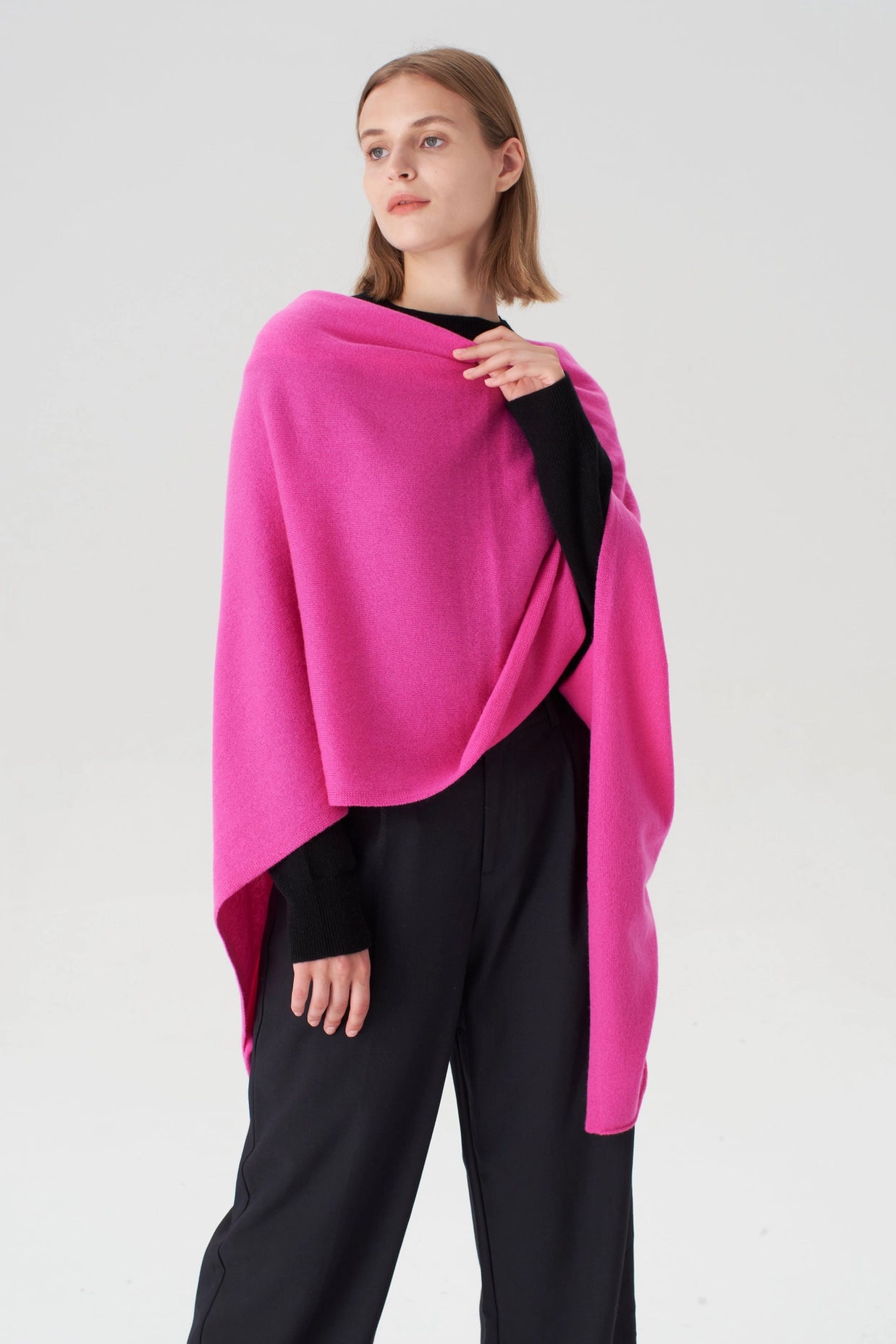 Bright fuchsia pink cashmere wrap shawl draped asymmetrically over black turtleneck and trousers on neutral background