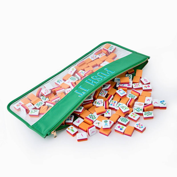 Mini mahjong set with colorful orange and white tiles with traditional symbols spilling from green vinyl zipper pouch