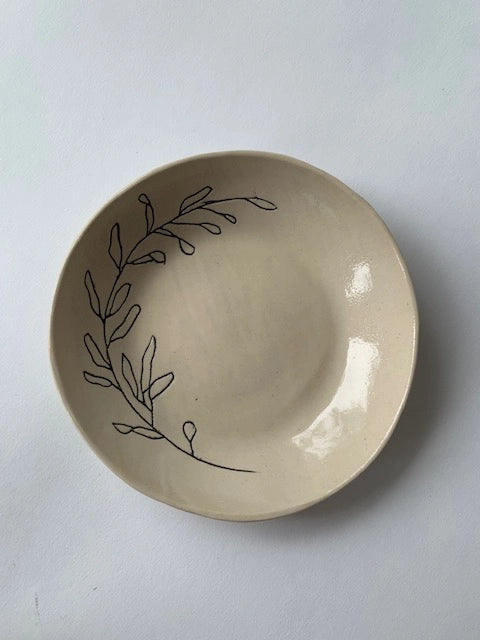 Cream ceramic bowl with hand-drawn black botanical leaf branch design along the rim, glossy glazed finish