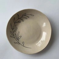 Cream ceramic bowl with hand-drawn black botanical leaf branch design along the rim, glossy glazed finish
