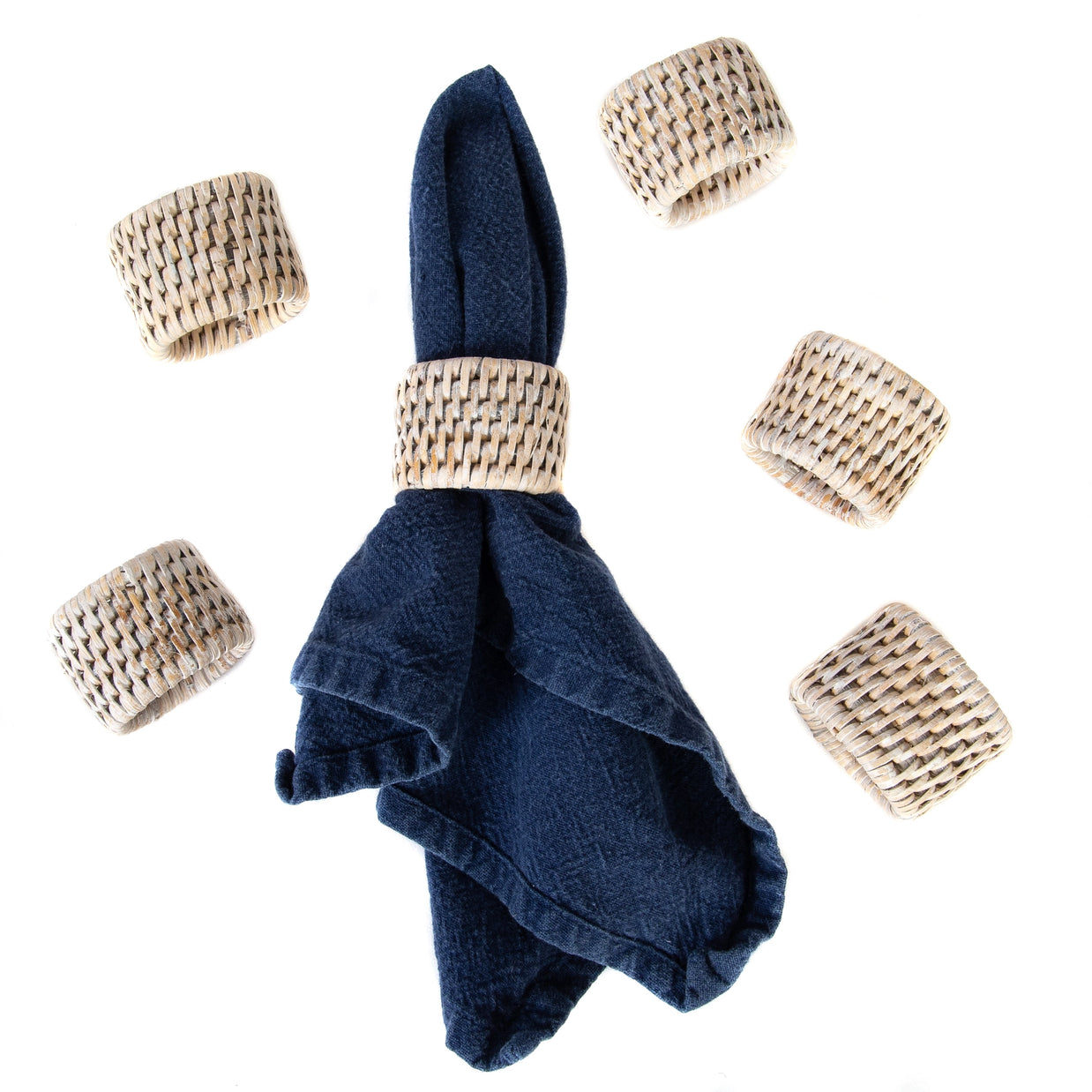 Navy blue linen napkin with woven natural rattan napkin ring surrounded by six matching basketweave rattan rings