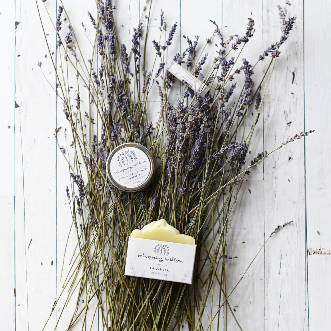Dried lavender bundle with pale purple blooms, small tin candle, and yellow handmade soap on white weathered wood