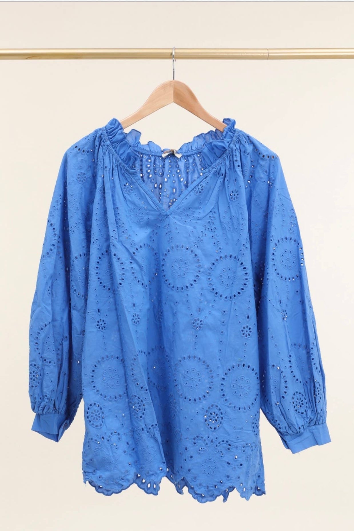 Cornflower blue cotton eyelet blouse with ruffle collar, puffed sleeves, and scalloped hem on wooden hanger