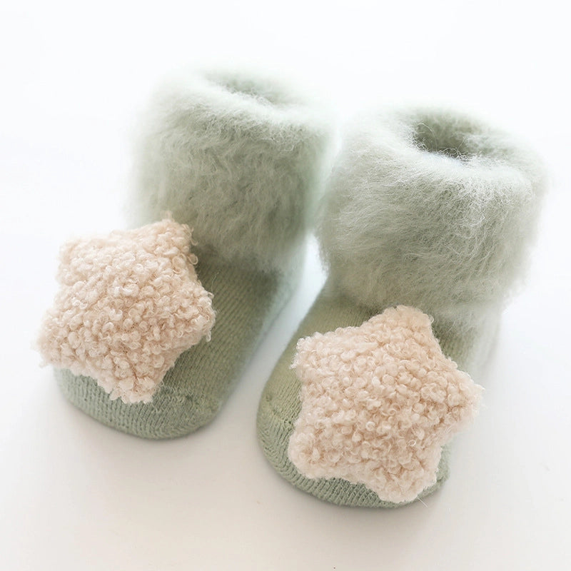 Sage green knit baby booties with fuzzy sherpa cuff and peach pompom toe detail on white background
