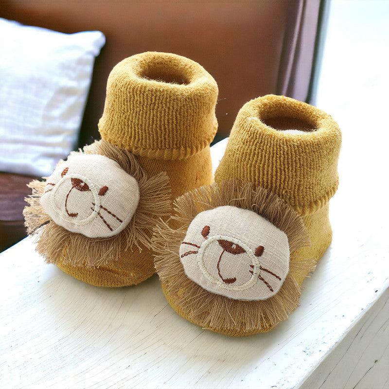 Mustard yellow baby booties with embroidered lion faces, fuzzy manes, and ribbed cuffs displayed on white surface